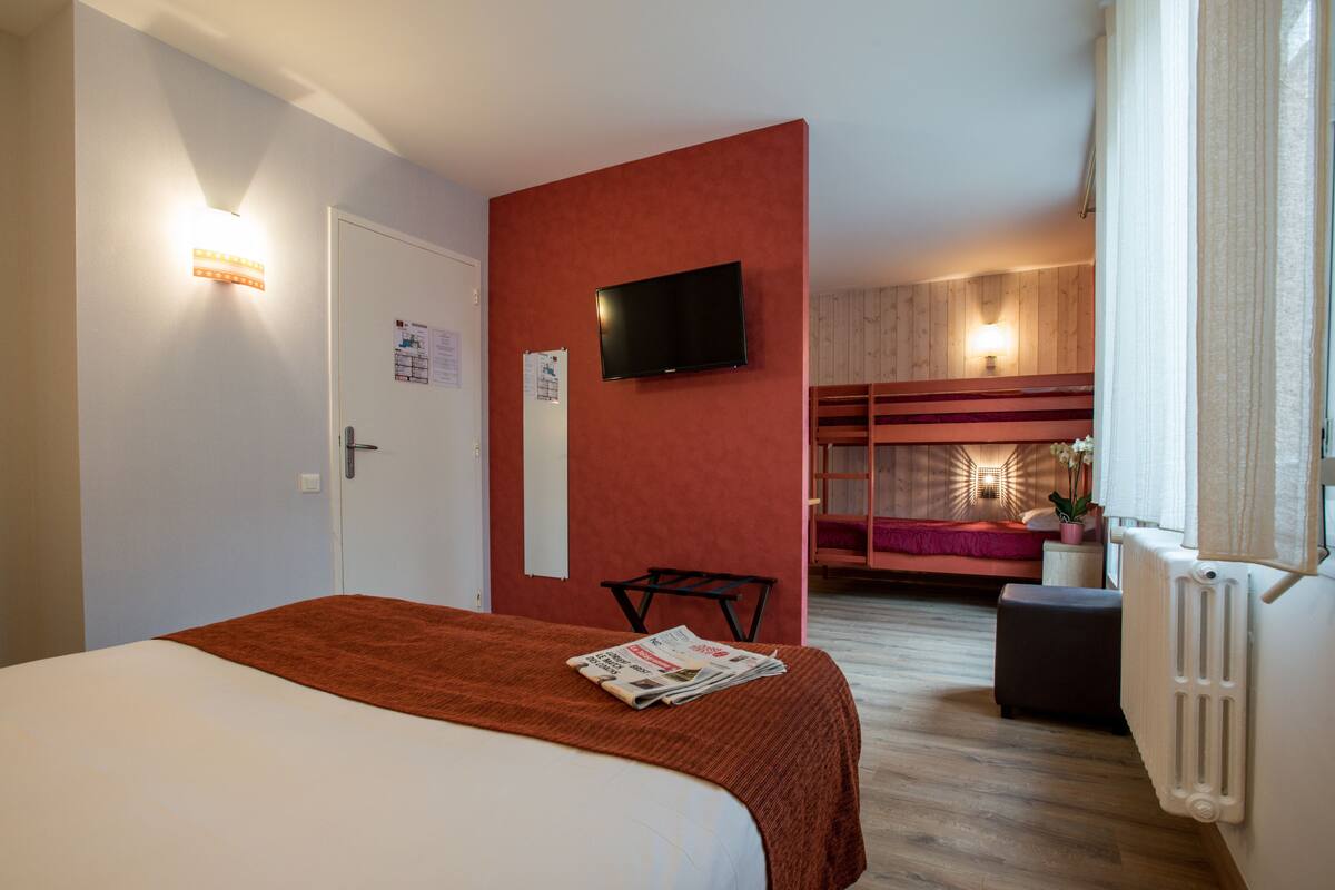 A hotel room with a bed, a television, a small table, and a seating area with a sofa and a chair.