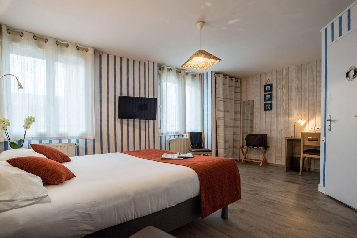 A hotel room with a large bed, a desk, a chair, a television, and a wooden floor.