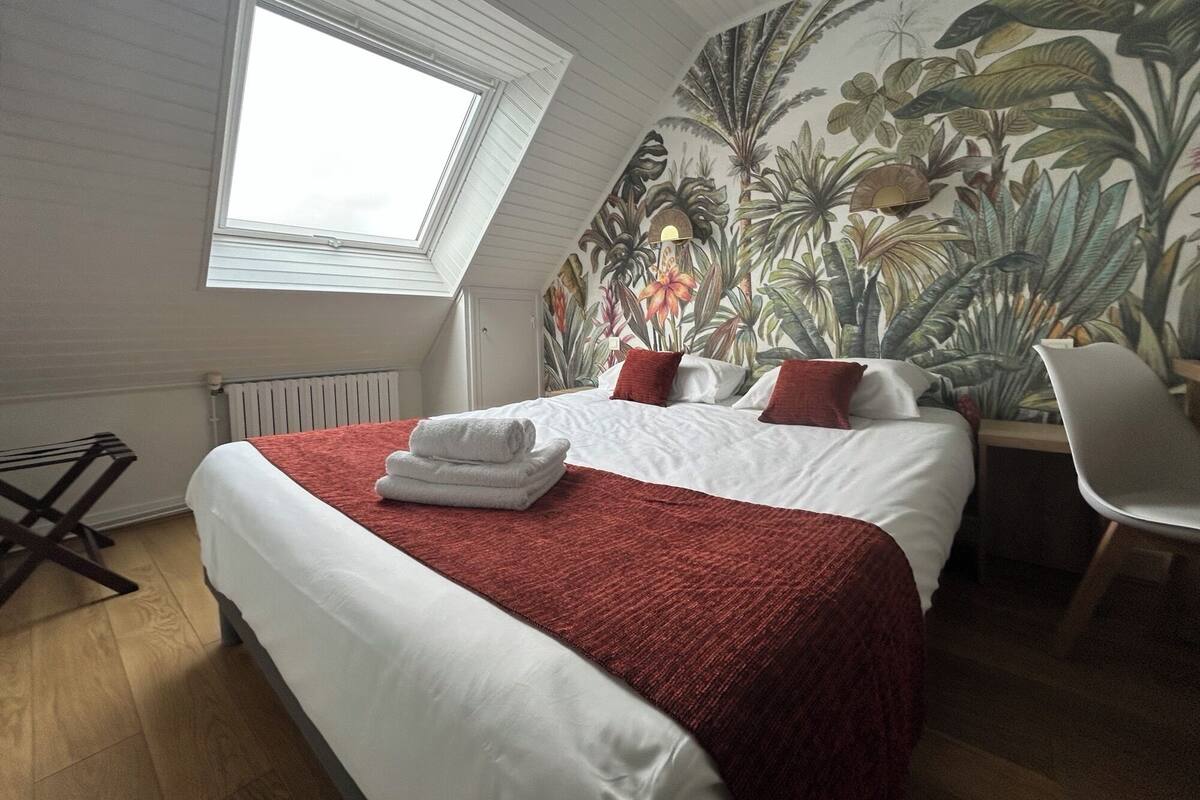 A bedroom with a large bed, a skylight, a tropical mural, and a chair.