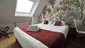 Un dormitorio con una cama grande, un tragaluz, un mural tropical y una silla.