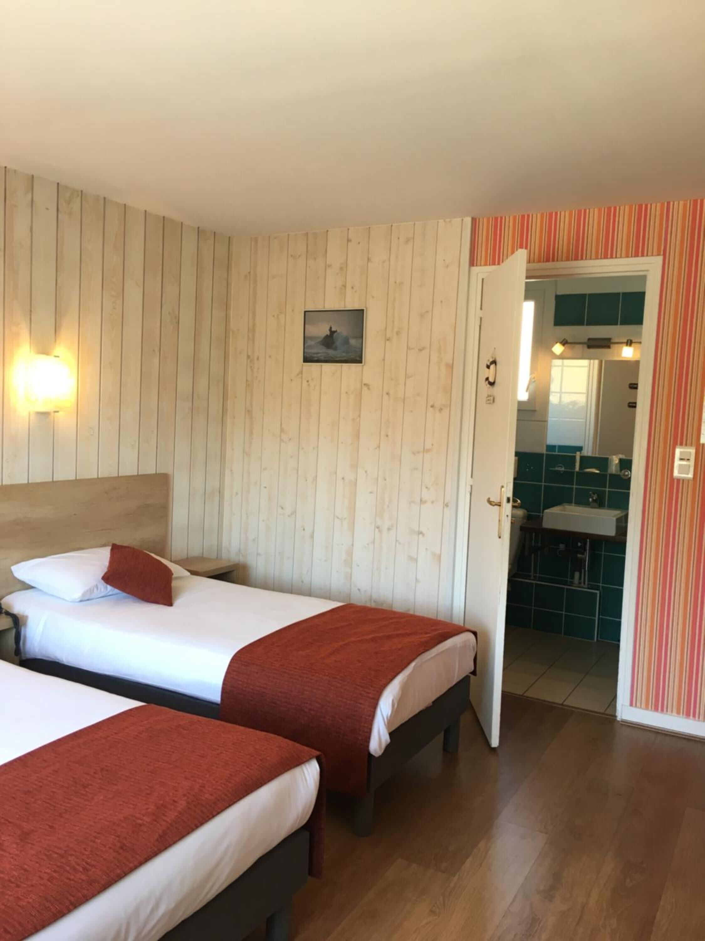 Una habitación con dos camas, paredes de madera, un cuadro pequeño y un baño visible a través de una puerta abierta.