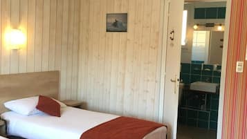 Una habitación con dos camas, paredes de madera, un cuadro pequeño y un baño visible a través de una puerta abierta.