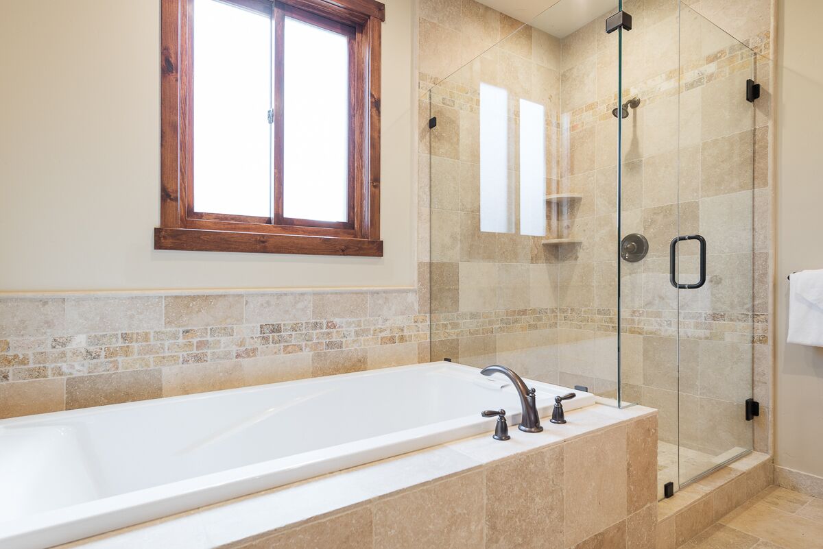 A modern bathroom with a large bathtub, a glass-enclosed shower, and a window above the tub.