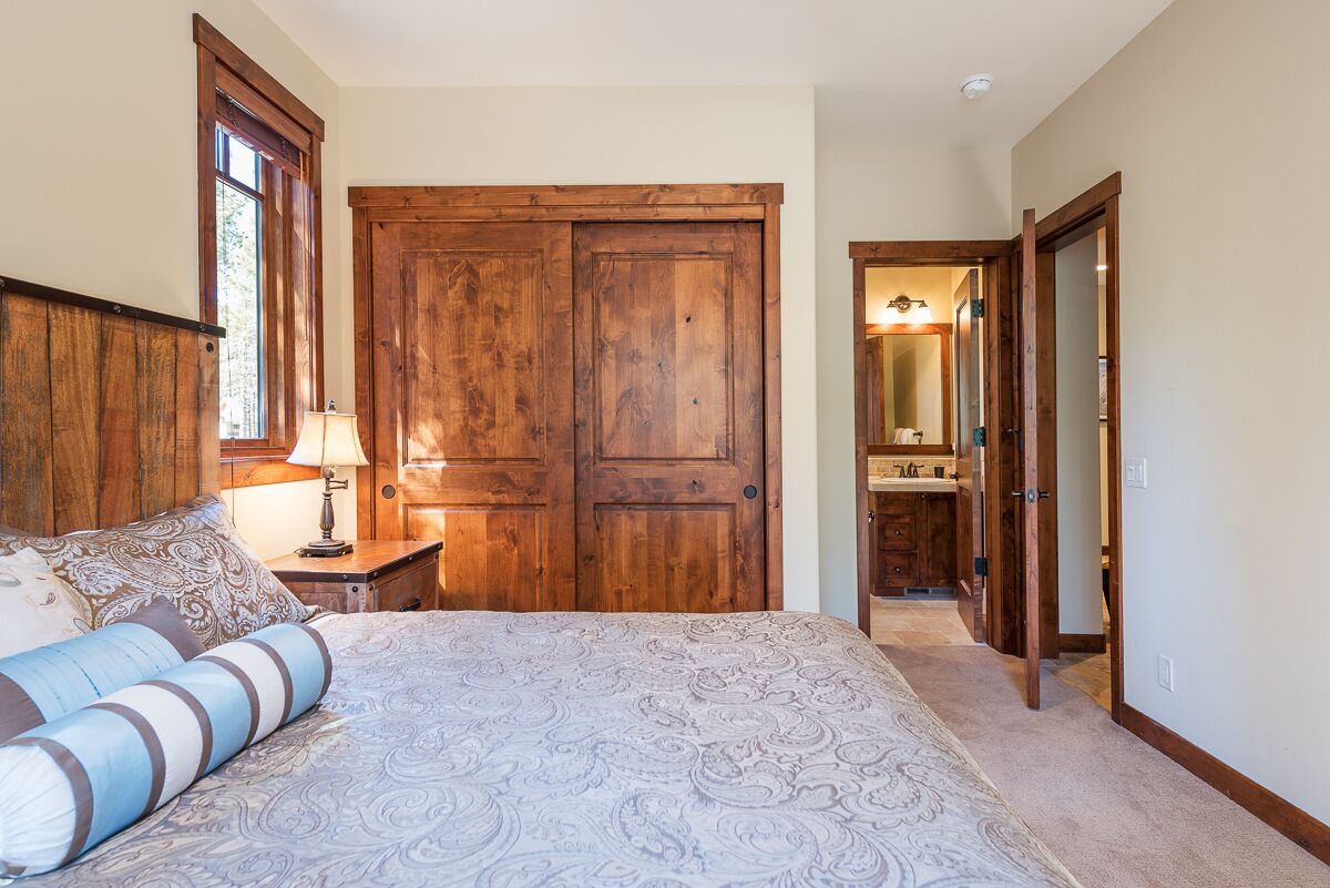 Een slaapkamer met een groot bed, een houten garderobe en een badkamer door een open deur zichtbaar.