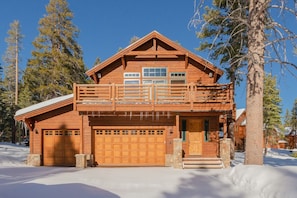 A two-story log cabin with a balcony, a garage, and a stone foundation.