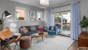 A modern living room with a grey sofa, a blue armchair, a brown leather chair, a wooden coffee table, and a large window with a view of a backyard. - Spacious remodeled Historical home - Family friendly &15 minutes to Everything! (St. Louis)
