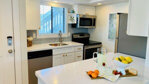 A modern kitchen with white cabinetry, stainless steel appliances, and a large island with fruit and a pitcher. - Beach Dune Retreat | 1BR w/ Bunks & Beach Service (Destin)