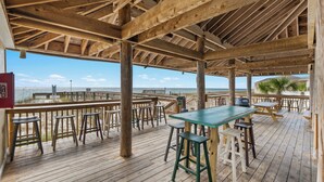 A wooden deck with tables and stools, overlooking a beach. - Beach Dune Retreat | 1BR w/ Bunks & Beach Service (Destin)