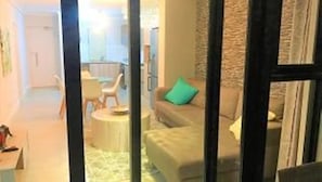 A room with a sofa, a small table, and a chair. There is a window with curtains.