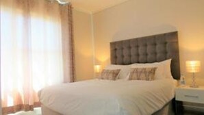A hotel room with a large bed, a nightstand, and a lamp. - Waters Edge 615 by CTHA (Cape Town)