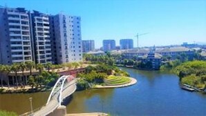 A river with a bridge, surrounded by greenery and modern buildings. - Waters Edge 615 by CTHA (Cape Town)