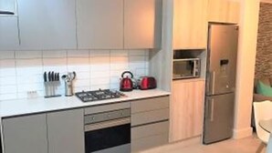 A modern kitchen with white cabinets, a microwave, a refrigerator, and a kettle on the counter. - Waters Edge 615 by CTHA (Cape Town)