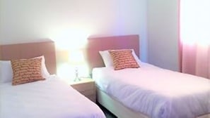 A hotel room with two single beds, each with a pillow and a nightstand.