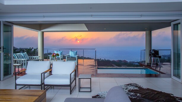 Un espacio moderno para disfrutar del aire libre con piscina, mobiliario y vistas al atardecer sobre el océano.