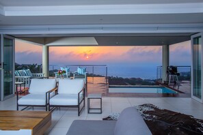 Ein moderner Außenbereich mit Pool, Sitzgelegenheiten und Blick auf den Sonnenuntergang über dem Meer.