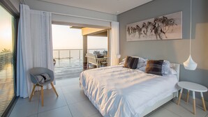 Un dormitorio moderno con una cama grande, una silla, una mesita y un balcón con vistas.
