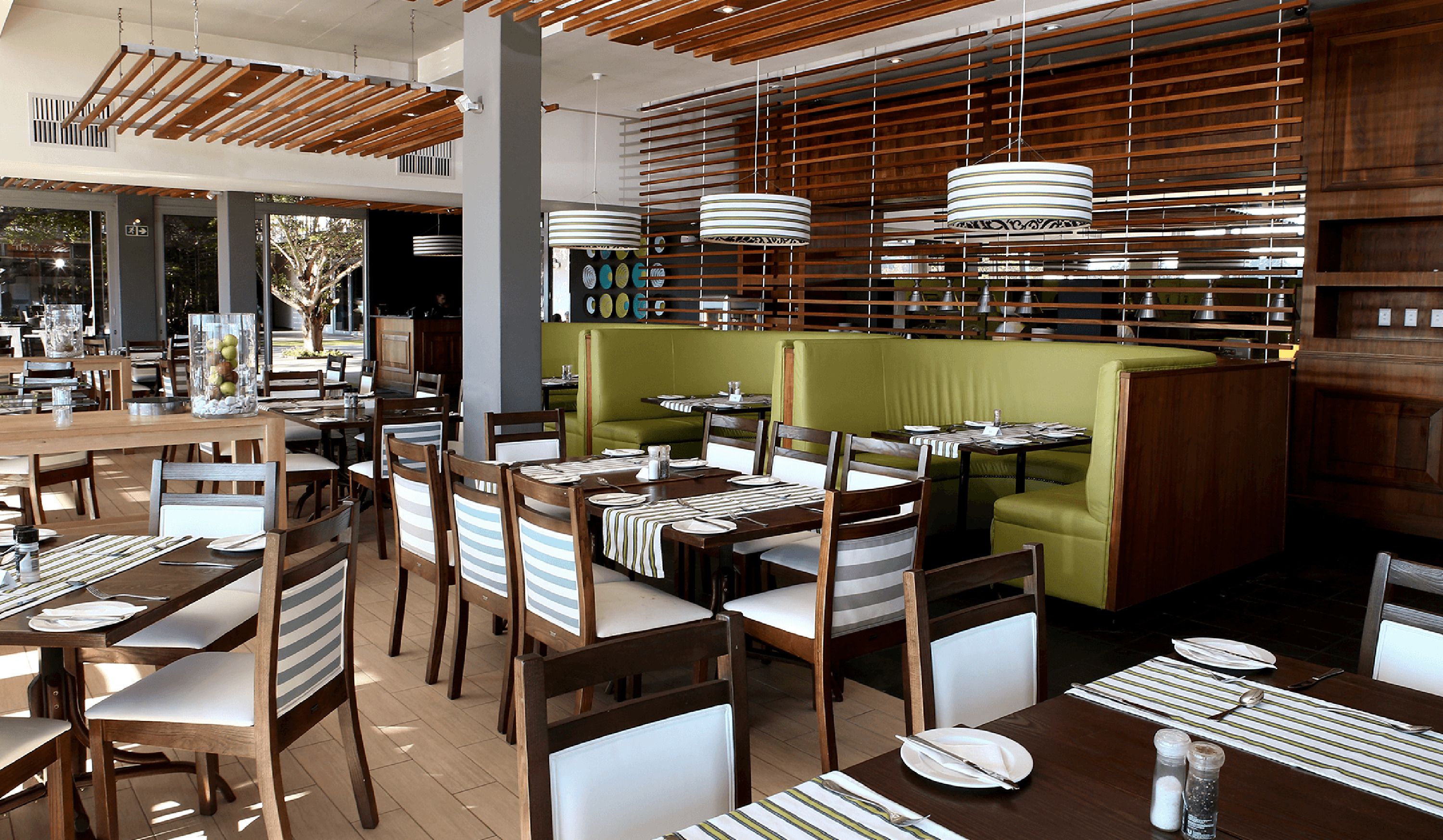 A restaurant interior with wooden tables and chairs, a green booth area, and hanging pendant lights.