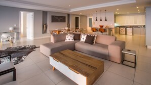 Una sala de estar moderna con un amplio sofá seccional, una mesa de centro de madera y un comedor con una mesa y sillas blancas.