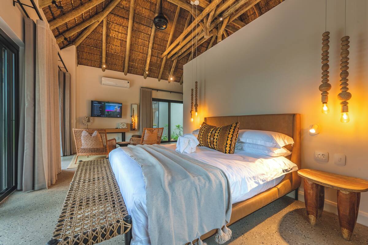 A spacious bedroom with a large bed, a wooden headboard, a small wooden table, and a TV on the wall.
