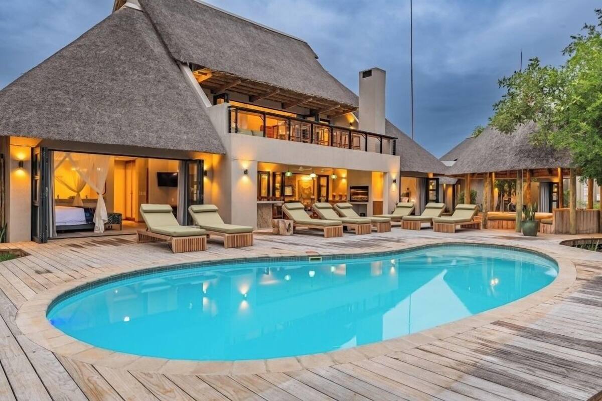 A resort with a swimming pool, lounge chairs, and thatched-roof buildings.