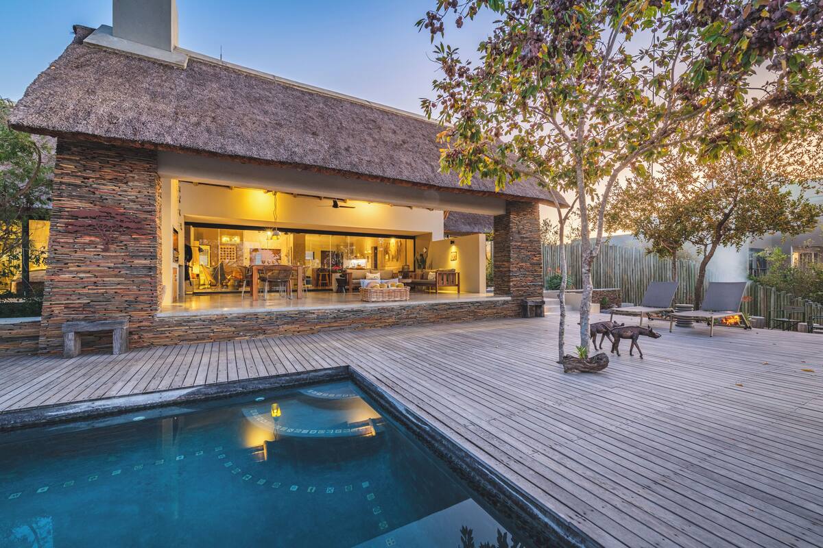 A modern house with a pool, outdoor seating, and a thatched roof.