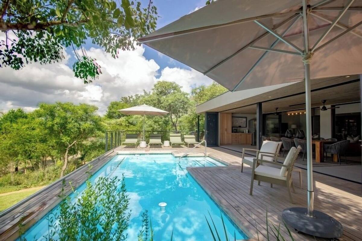 A modern outdoor pool area with a wooden deck, lounge chairs, and umbrellas.