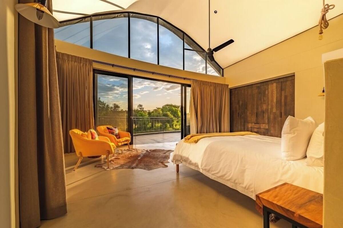 A spacious bedroom with a large bed, a ceiling fan, and a view of the outdoors through a sliding glass door.