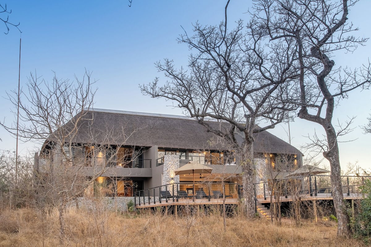 A modern two-story house with a stone facade, large windows, and a balcony with outdoor seating.