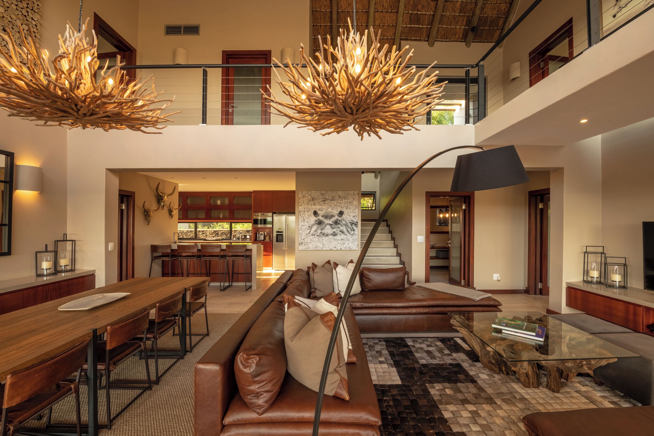 A spacious living area with a high ceiling, a dining table, a sofa set, and a staircase leading to an upper level.