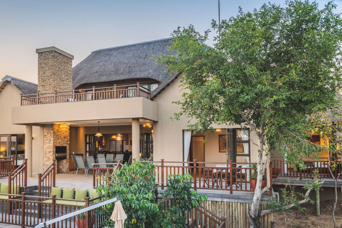 A two-story house with a stone fireplace, outdoor seating, and a balcony.