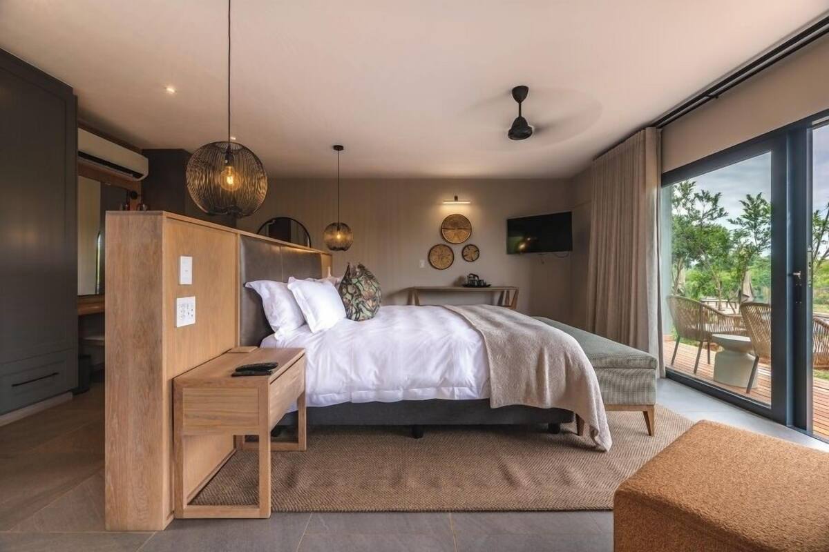 A modern bedroom with a bed, bedside tables, a wardrobe, a TV, and a balcony with outdoor furniture.