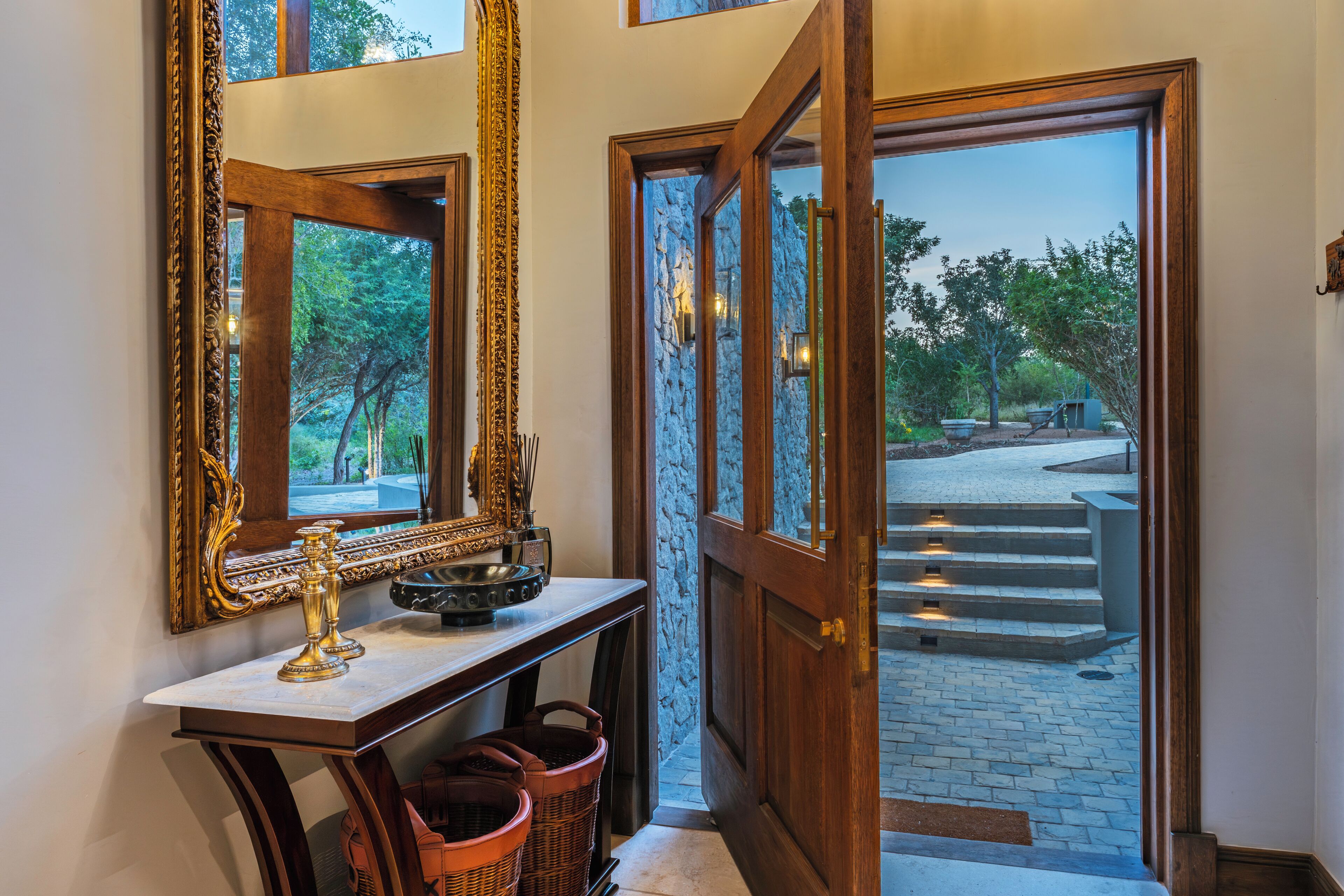 A hallway with a mirror, a wooden door, and a view of the outside.