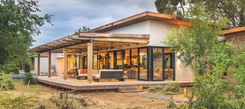 Una casa moderna con un porche cubierto, un comedor y una cocina visibles a través de amplios ventanales.