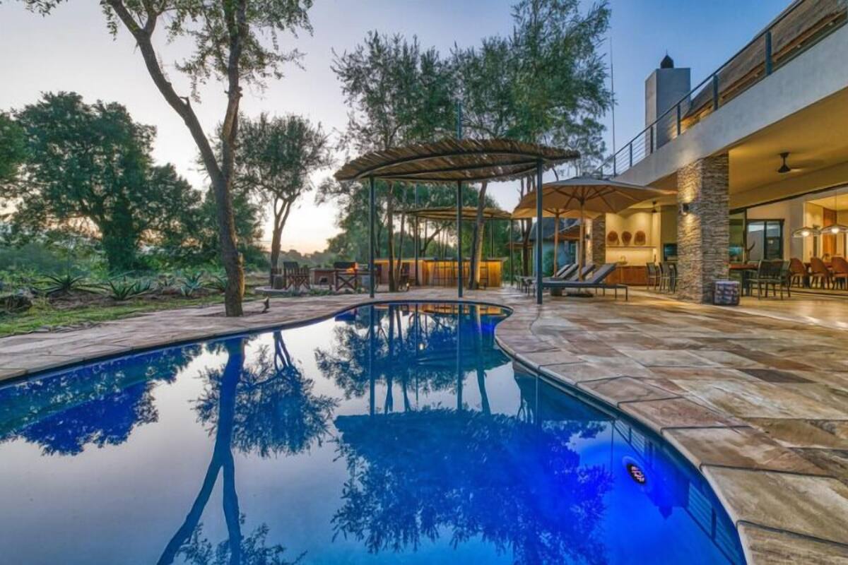 A swimming pool with a pergola, outdoor seating, and a stone patio.