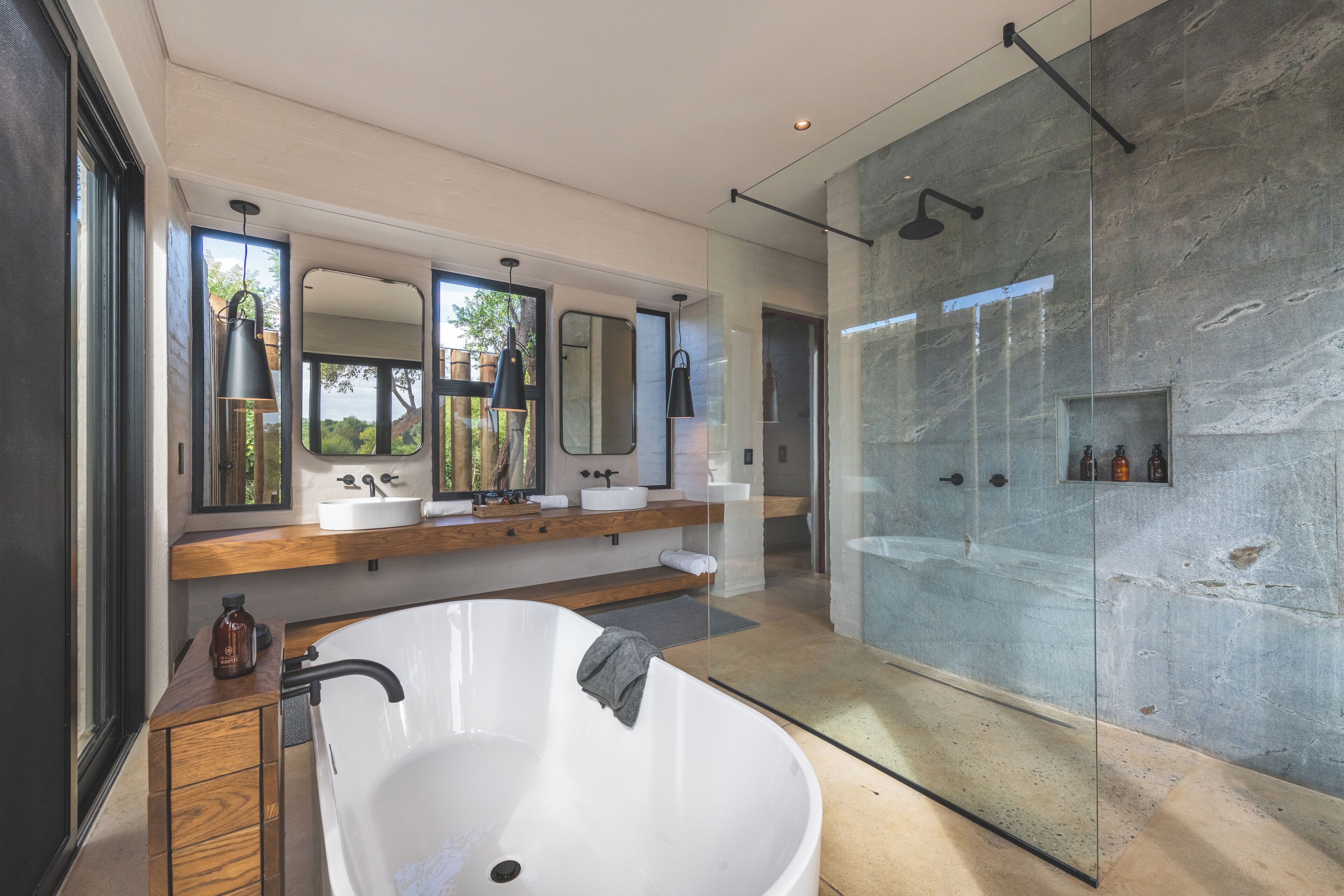 Un baño moderno con una bañera independiente, ducha con mampara de vidrio y un espejo grande sobre el lavamanos.