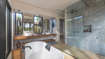 Un baño moderno con una bañera independiente, ducha con mampara de vidrio y un espejo grande sobre el lavamanos.