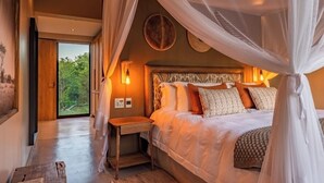 Une chambre à coucher avec un grand lit, une table de chevet, une commode et une fenêtre donnant sur un paysage verdoyant.