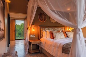 Un dormitorio con una cama grande, una mesita de noche y un ventanal con vistas a la vegetación.