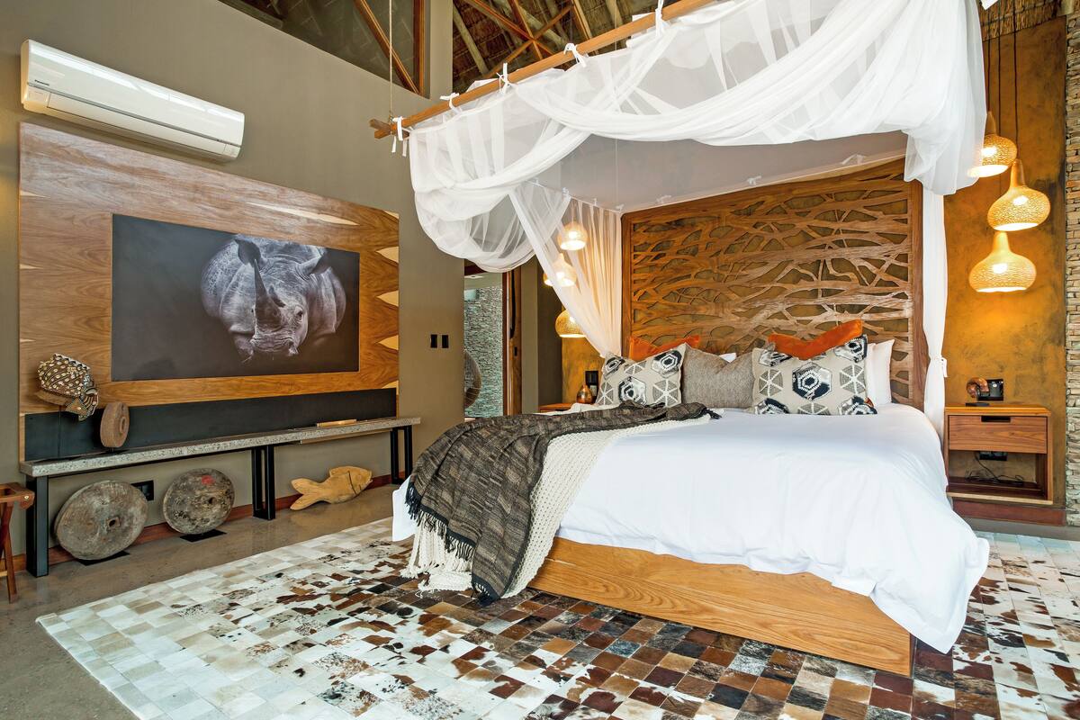 A bedroom with a large bed, a canopy, a mounted TV, and a unique wall design.