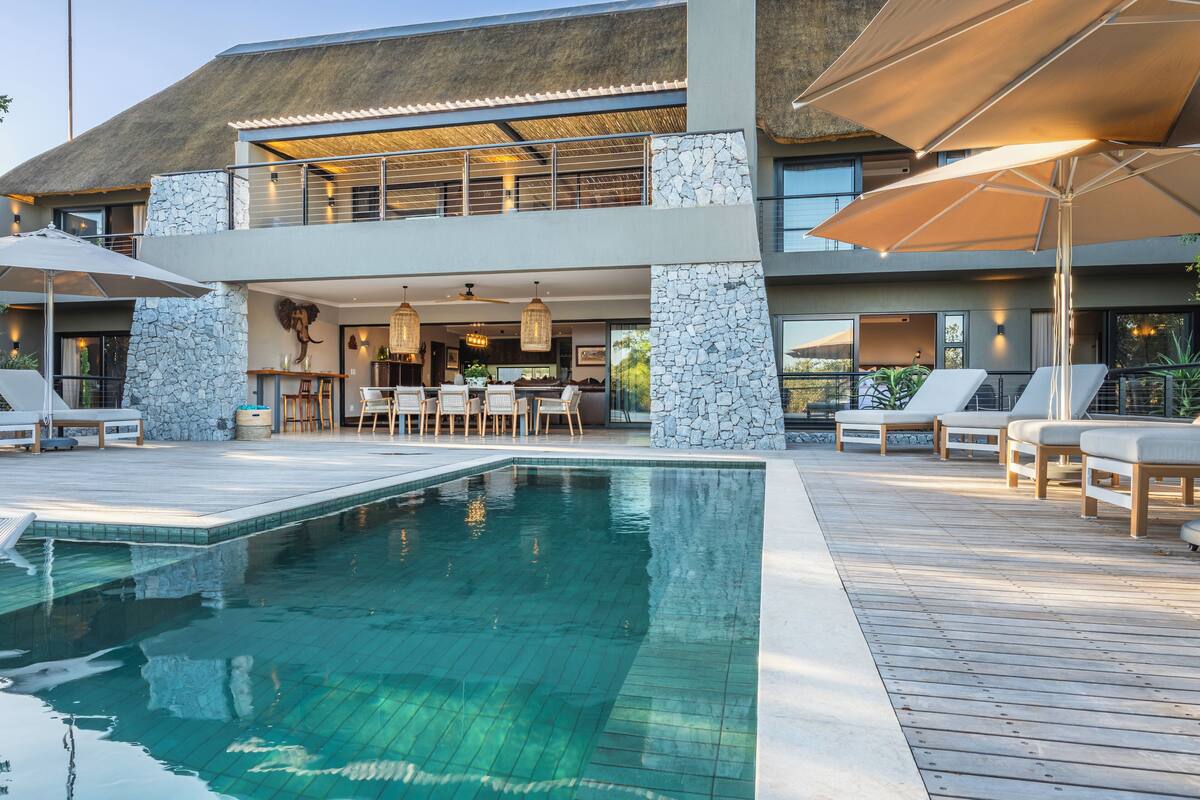 A modern house with a swimming pool, outdoor seating, and a stone facade.