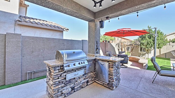 Une cuisine extérieure dotée d’un barbecue encastré, d’éléments décoratifs en pierre et d’un parasol rouge.