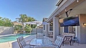 Une terrasse extérieure avec une table et des chaises en verre, une piscine et un téléviseur fixé au mur.