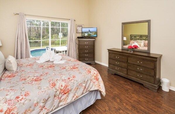A bedroom with a bed, a dresser, a television, and a view of a swimming pool.
