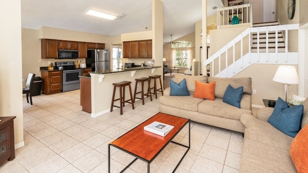 Un salón amplio con sofá y mesa de centro, una cocina con armarios de madera y electrodomésticos, y una escalera que sube a un nivel superior.