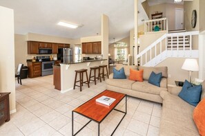 A spacious living room with a sofa and coffee table, a kitchen with wooden cabinets and appliances, and a staircase leading to an upper level.