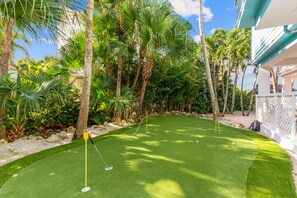 Ein Golfplatz mit Putting-Green, umgeben von Palmen und einem weißen Zaun.