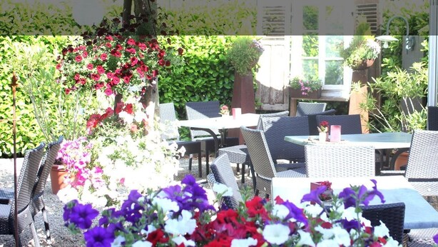 An outdoor patio with wicker furniture, potted plants, and a view of a house in the background. - Hotel Gasthaus Gellenberg (Rehlingen-Siersburg)