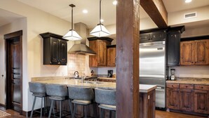A kitchen with dark wooden cabinets, a stainless steel refrigerator, and a central island with bar stools.