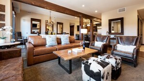 A spacious living room with a brown leather sofa, a wooden coffee table, and leather armchairs.