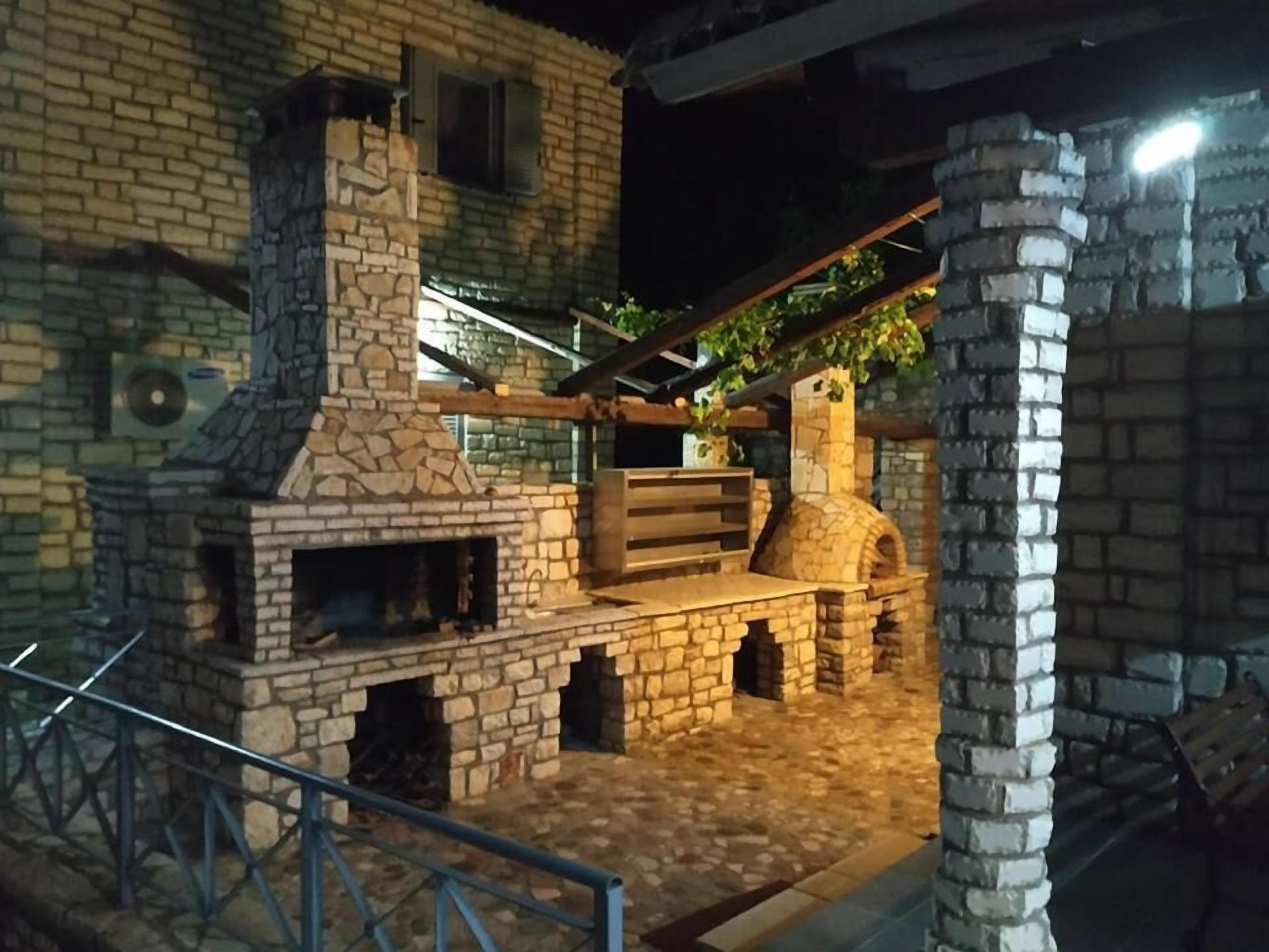 Un edificio de ladrillo con chimenea de piedra, un banco de madera y una pérgola cubierta de plantas trepadoras.